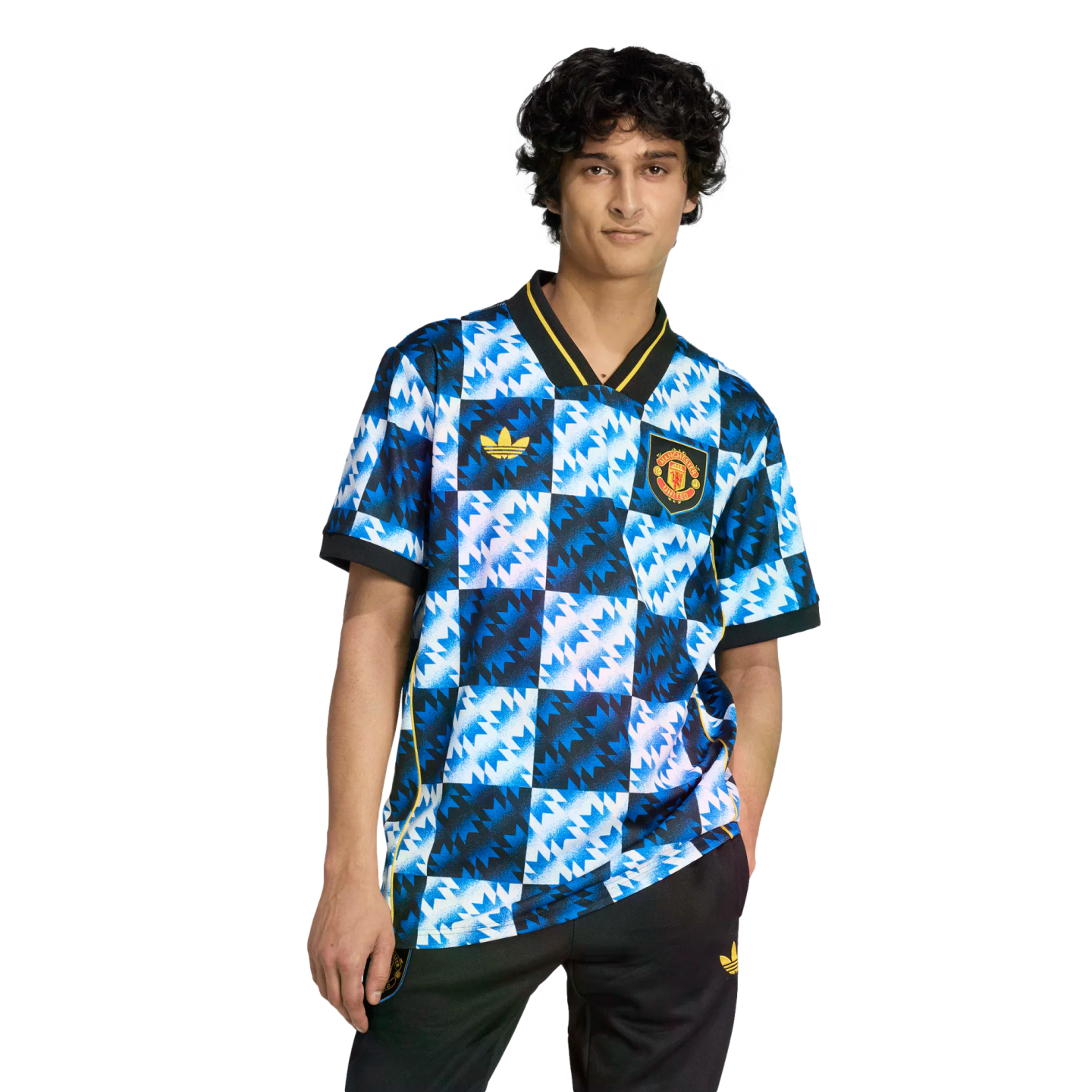 A person wearing a blue and white zig-zag patterned Manchester United soccer jersey and black pants, standing against a black background.