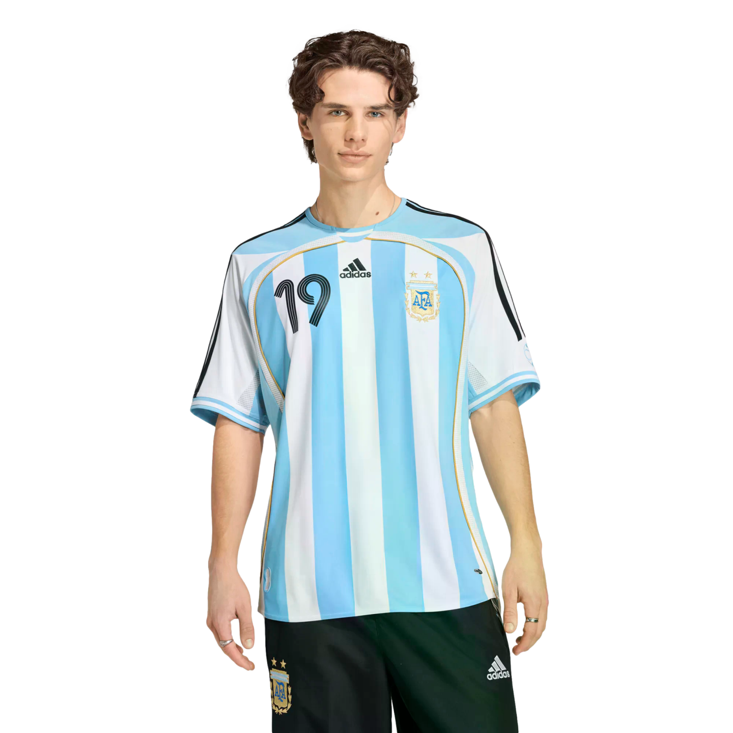 A young man with curly brown hair wearing a blue and white striped Argentina football jersey and black shorts against a black background.