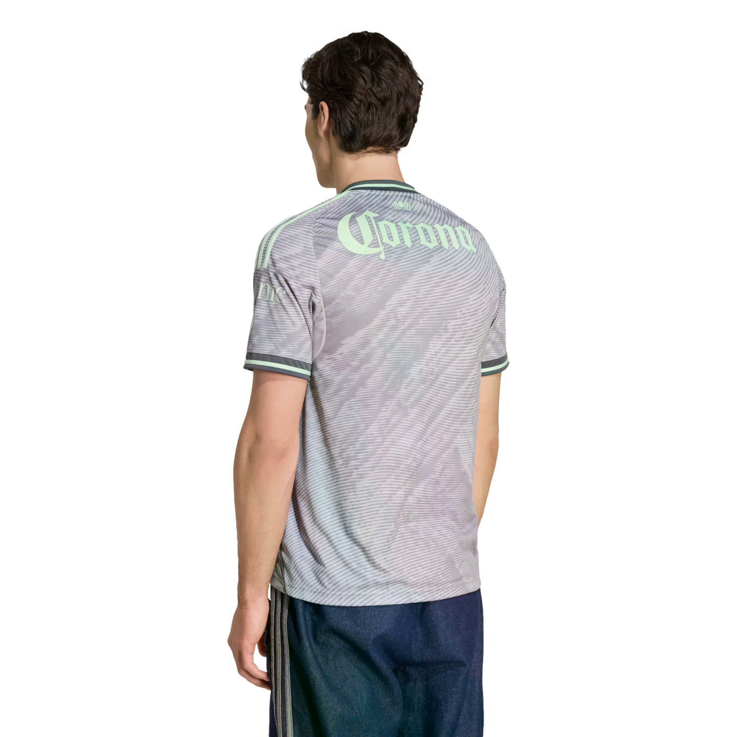 Back view of a man in a gray patterned jersey with "Corona" in mint green lettering and dark blue shorts, set against a black background.