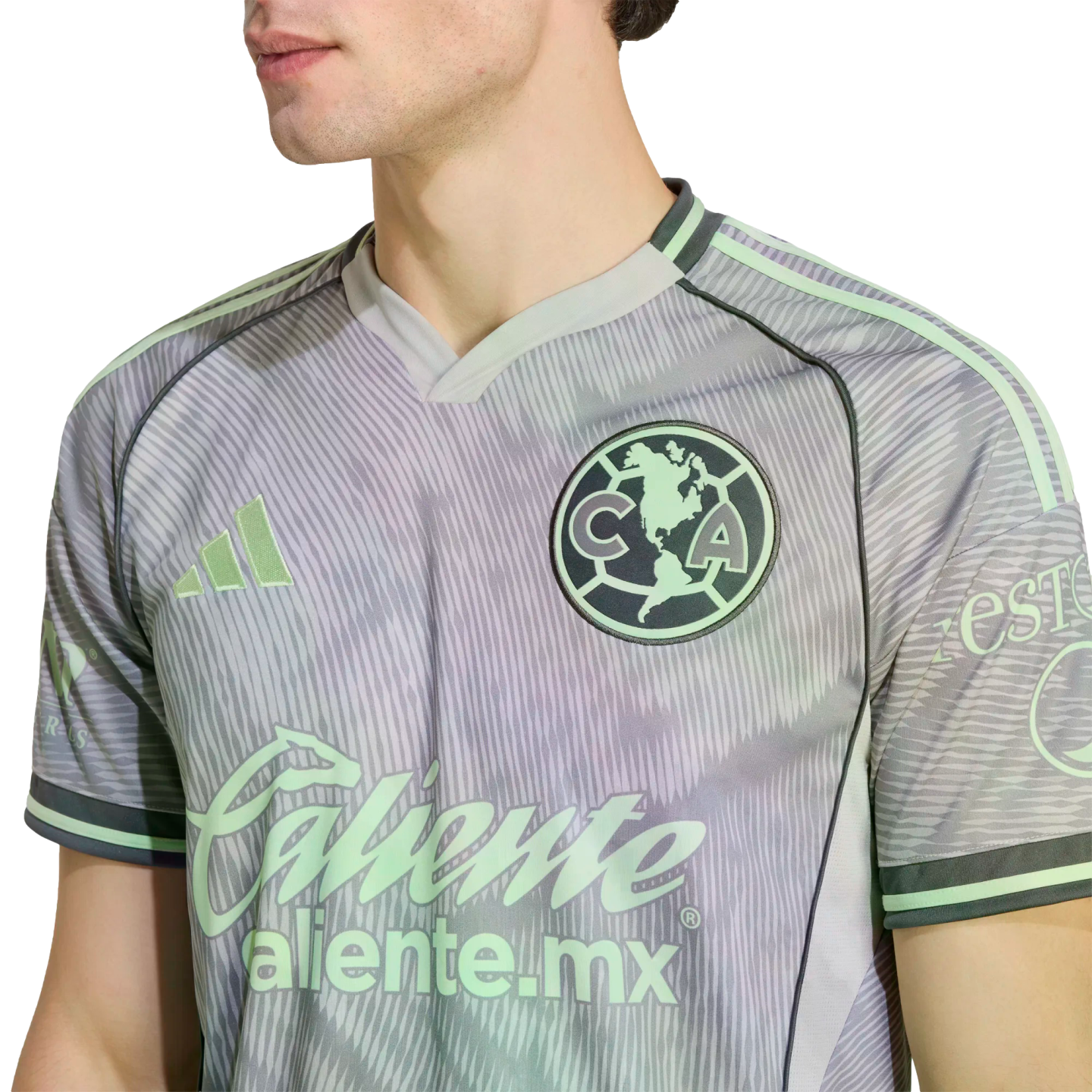 Close-up of a man wearing a grey and pale green Adidas Club América soccer jersey with the team crest and Caliente sponsor logo.