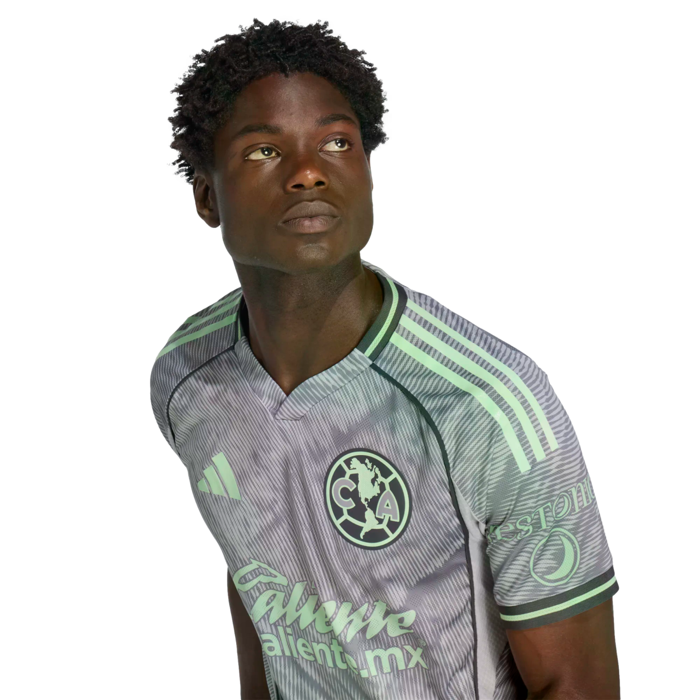 Portrait of a young Black man wearing a grey and lime green Club América soccer kit, gazing upwards. The background is solid black.