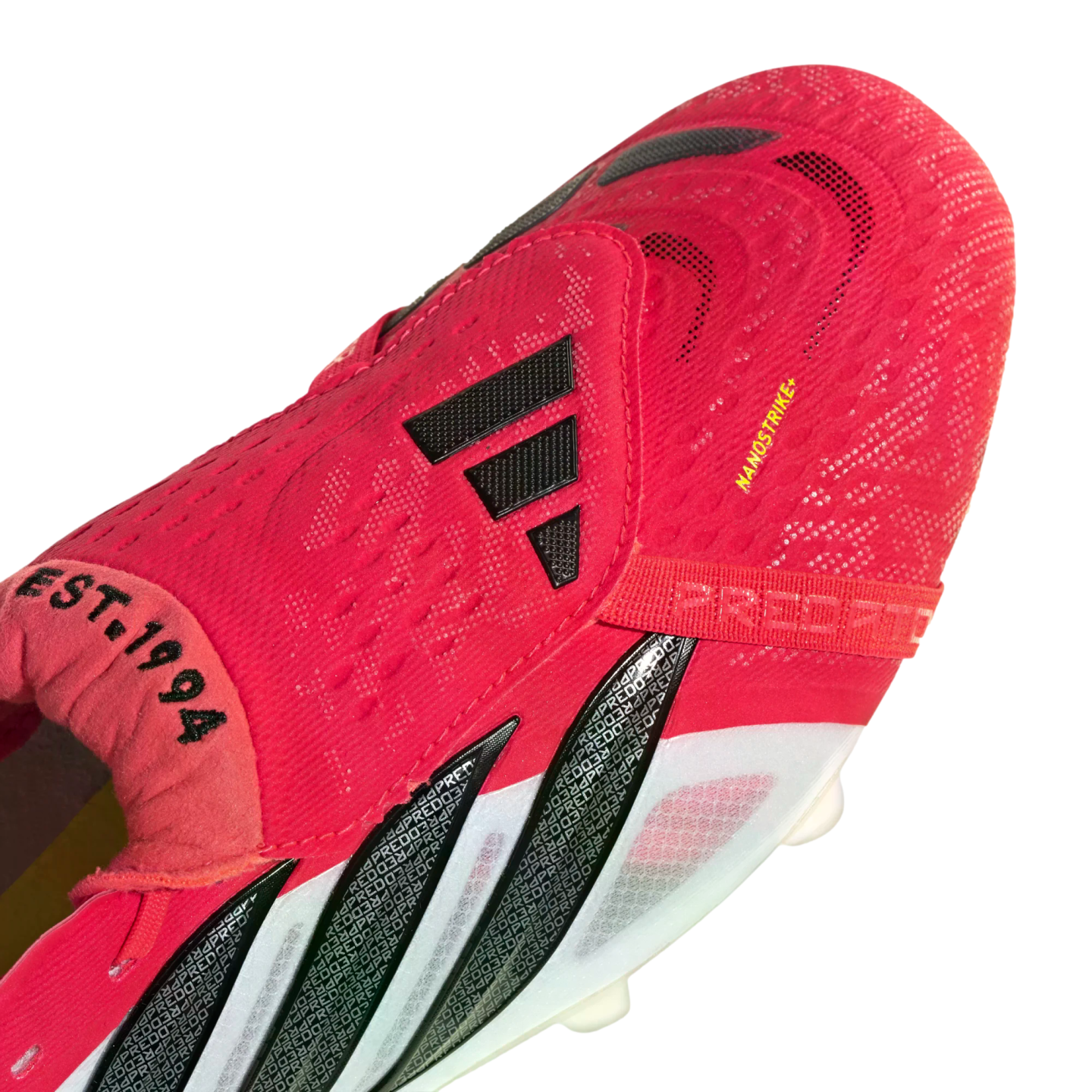 Close-up of a red Adidas Predator soccer cleat with black stripes, white side accents, and the text "EST. 1994" and "NANOSTRIKE+".