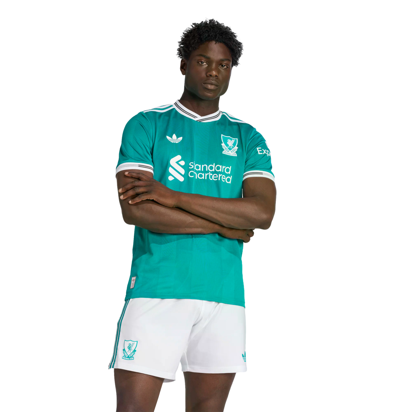 A man models a teal Liverpool FC soccer jersey with white trim and matching white shorts, featuring the Adidas Originals and Standard Chartered logos against a black background.