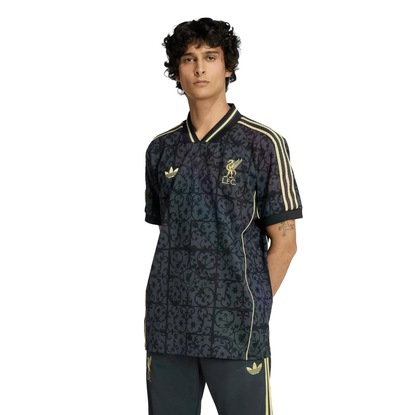 A male model wearing a dark, patterned Liverpool FC x Adidas jersey with gold accents and matching pants against a black background.