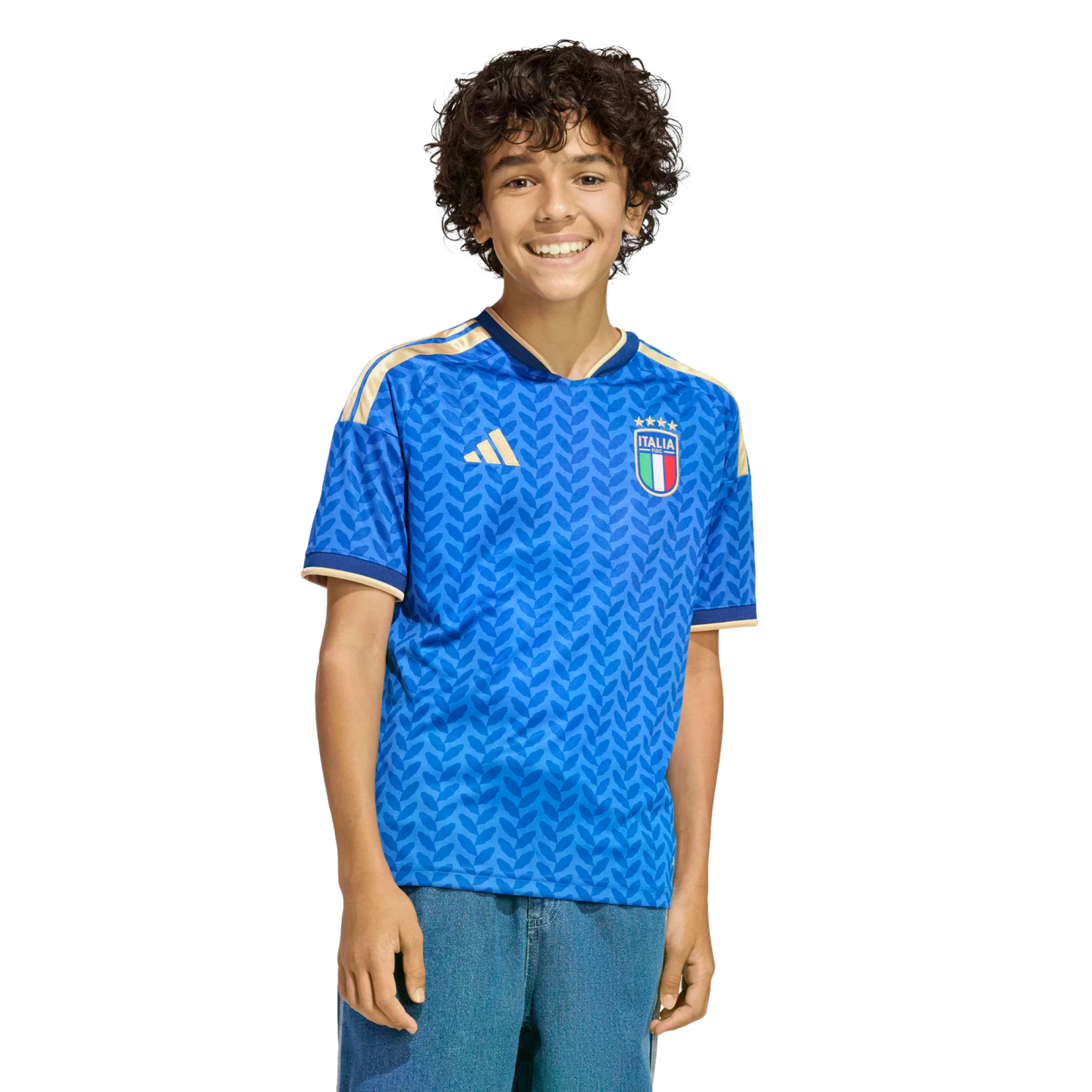 A smiling boy with curly hair wearing a blue patterned Italy soccer jersey and blue jeans, standing against a black background.