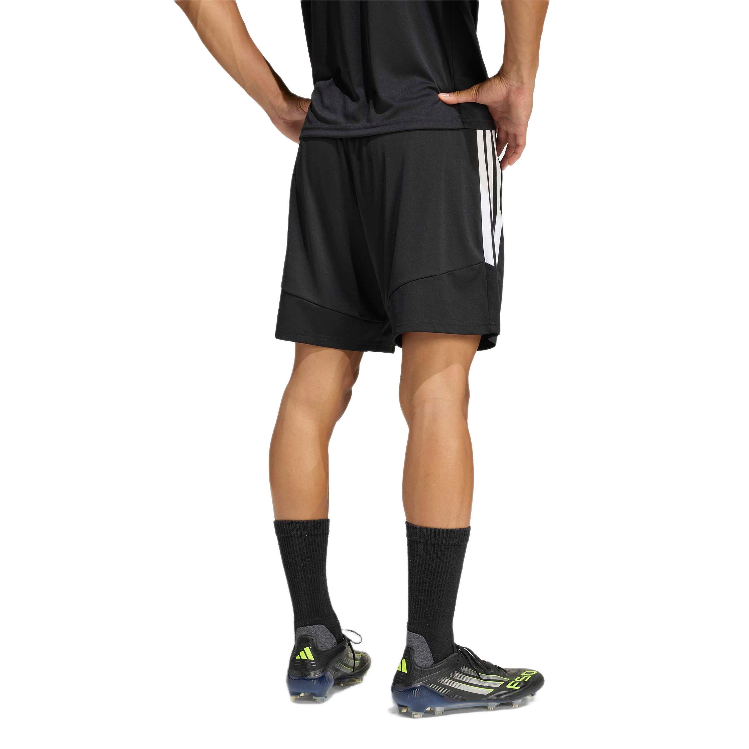 Rear view of a person wearing black Adidas athletic shorts, a black shirt, and soccer cleats against a plain white background.