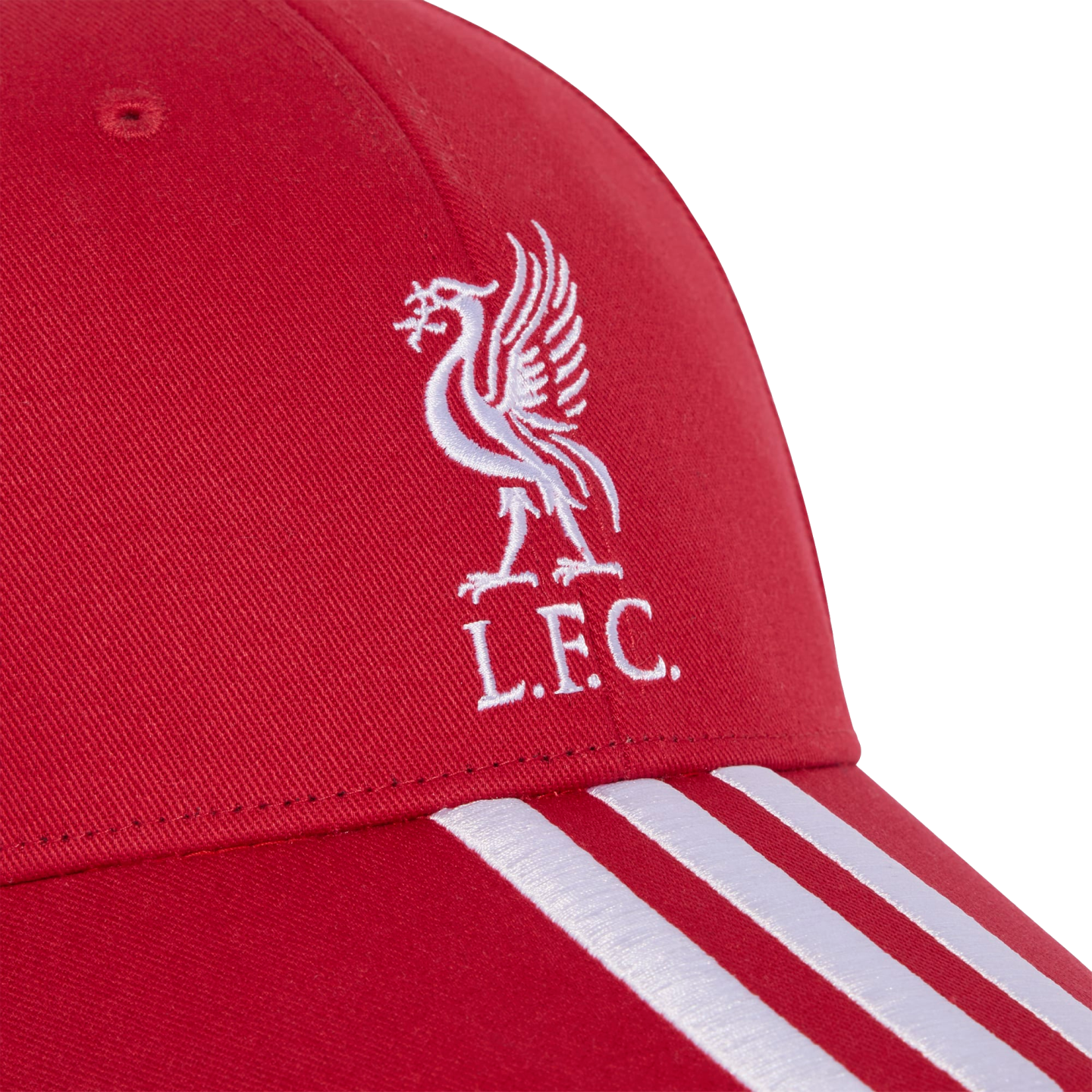 Close-up of a red baseball cap with a white embroidered Liverpool FC Liver Bird logo and "L.F.C." text, featuring three white stripes on the brim.