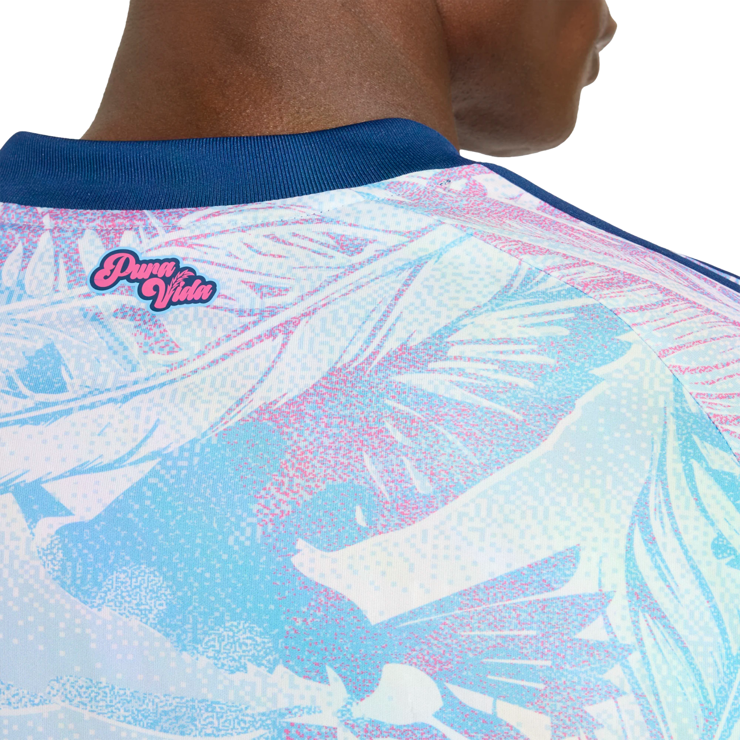 Close-up of a person's upper back wearing a light blue and pink tropical print jersey with a navy blue collar and a pink "Pura Vida" logo.