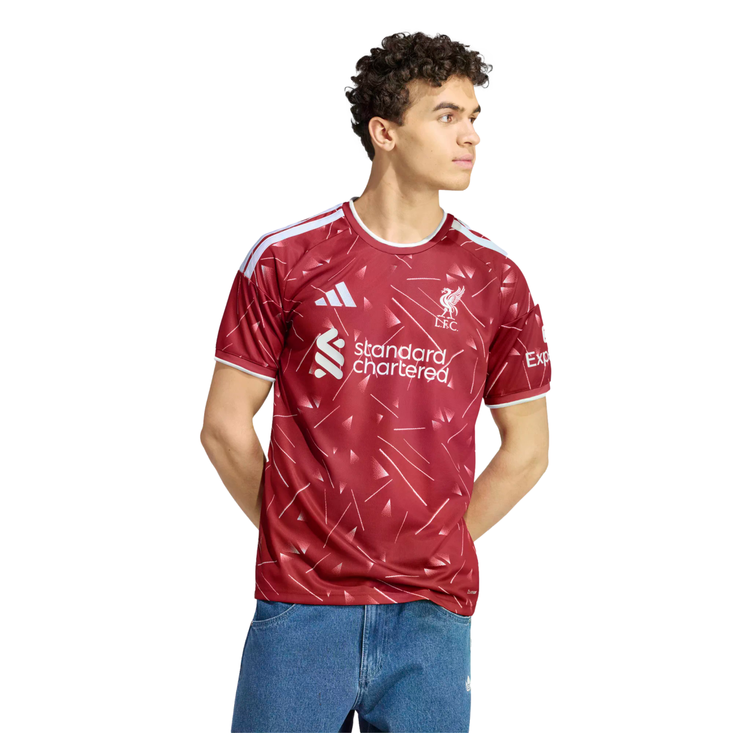 A man with curly hair wearing a red and white Liverpool FC soccer jersey and blue jeans, standing against a white background.