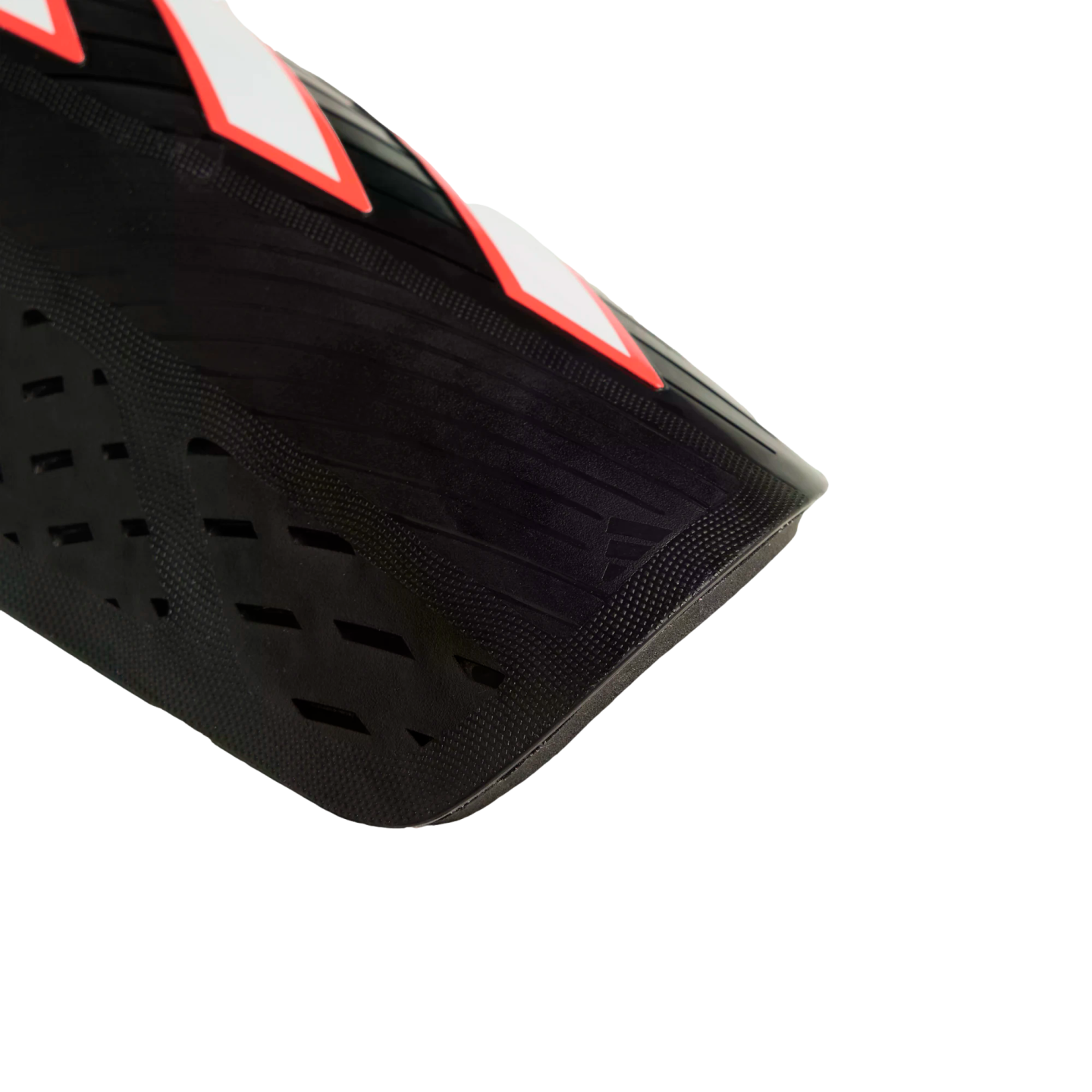 Close-up of a black shin guard with red and white accents, featuring perforated and ridged textures against a black background.