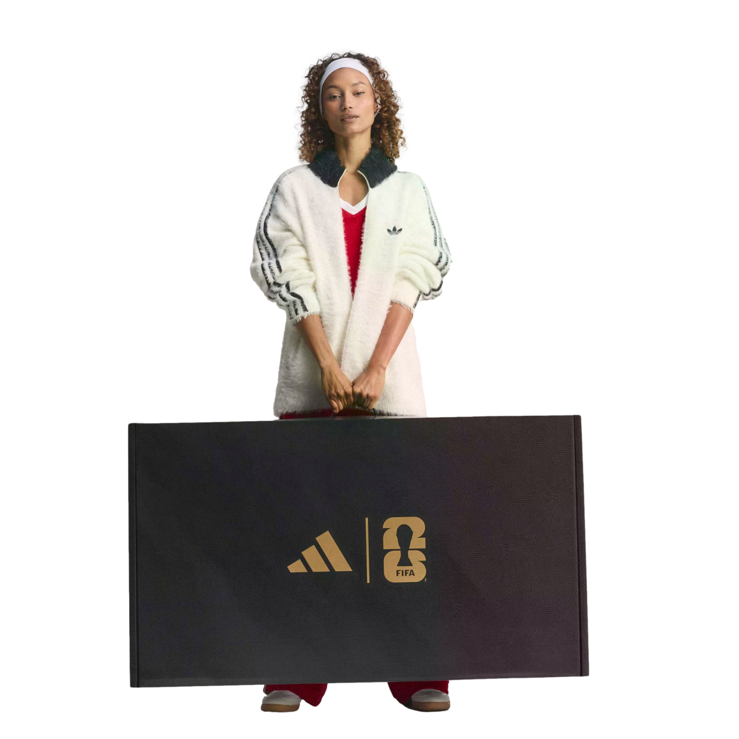 A woman in a white Adidas jacket holds a large black box featuring gold Adidas and FIFA World Cup 26 logos.