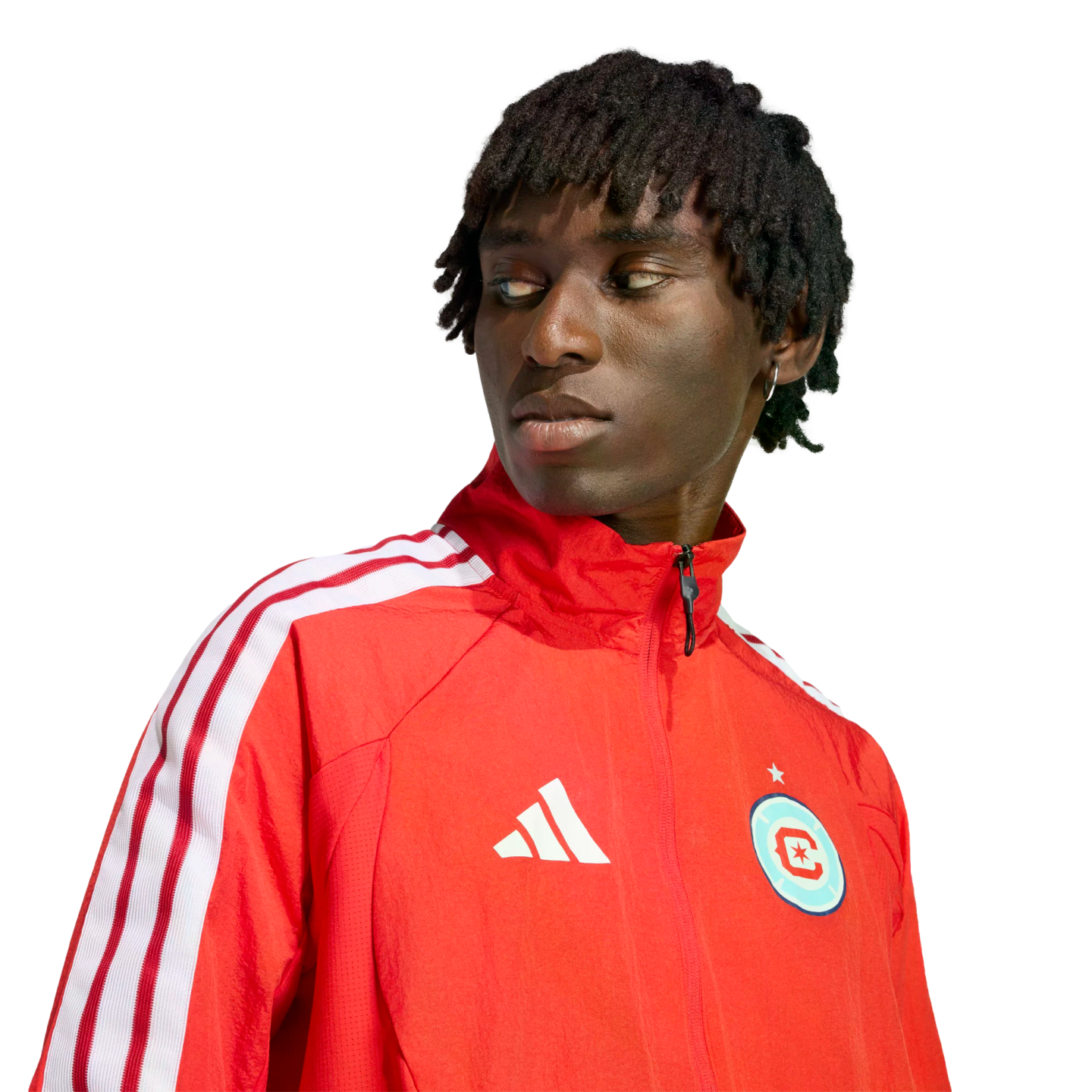 A man with short dreadlocks wearing a red Adidas track jacket with white stripes, looking off-camera against a black background.