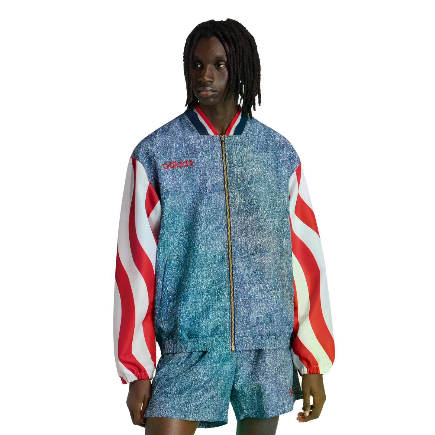 A person with dreadlocks models a blue acid-wash Adidas jacket with red and white wavy striped sleeves and matching shorts against a black background.