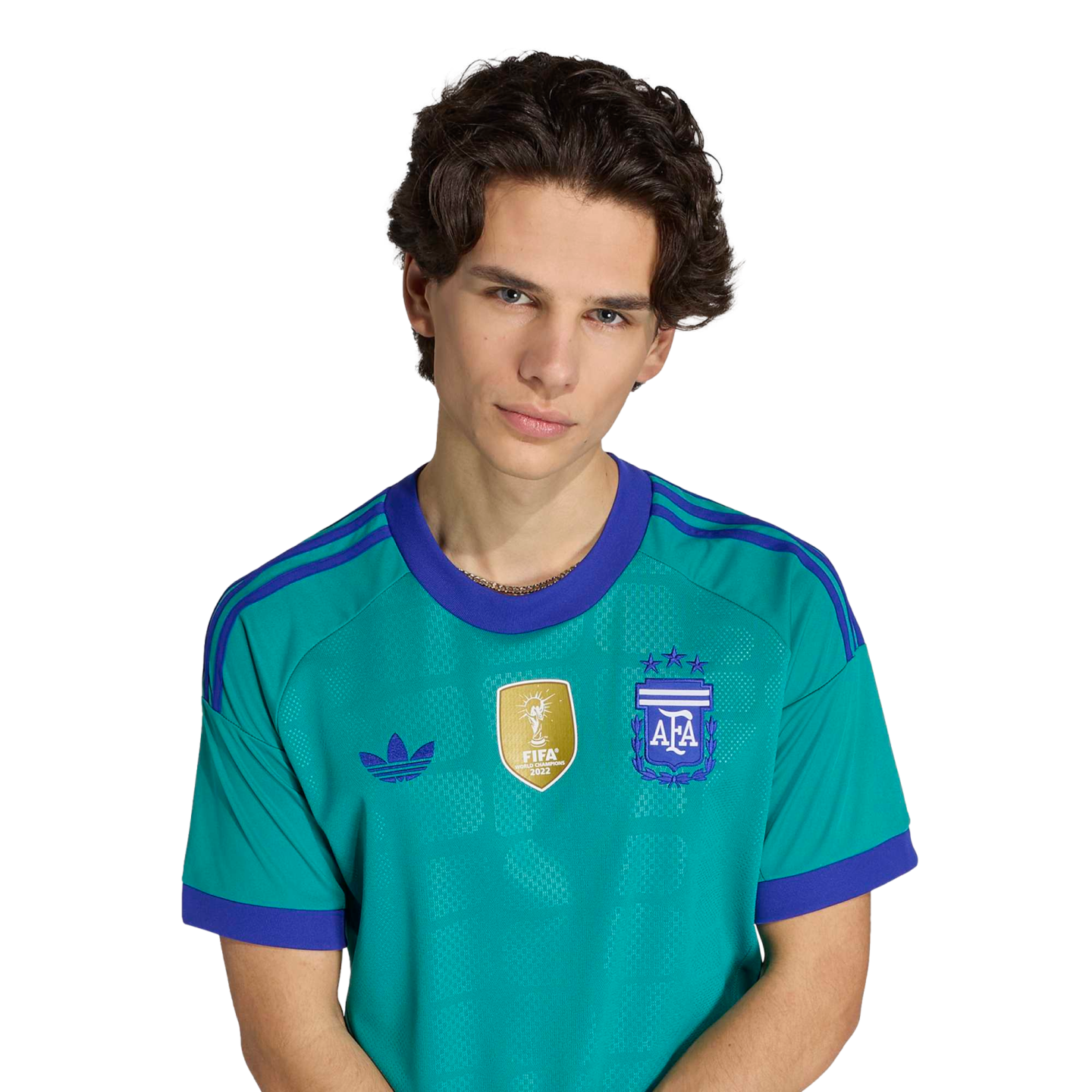Portrait of a young man with wavy brown hair wearing a teal Argentina national team jersey with purple details and a gold FIFA patch against a black background.