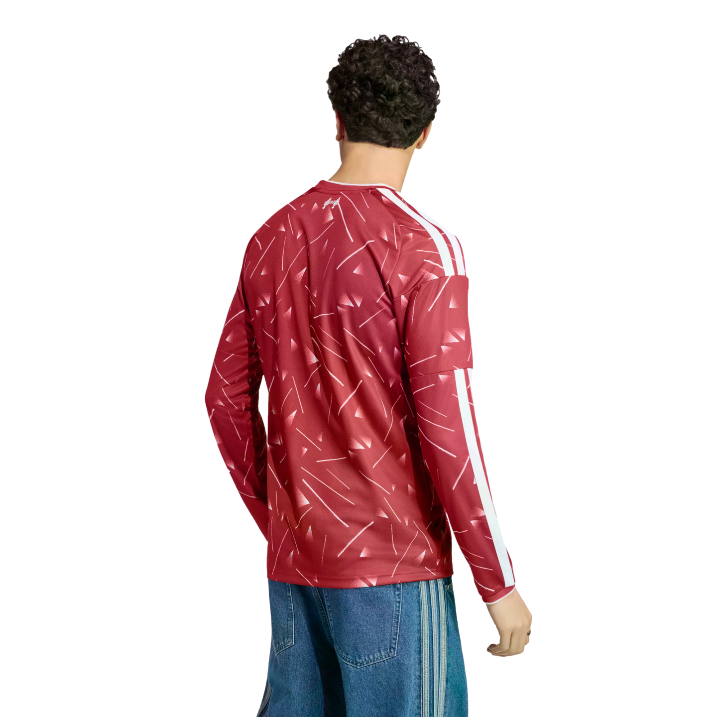 Rear view of a man wearing a red patterned long-sleeve jersey with white stripes and blue denim jeans against a white background.