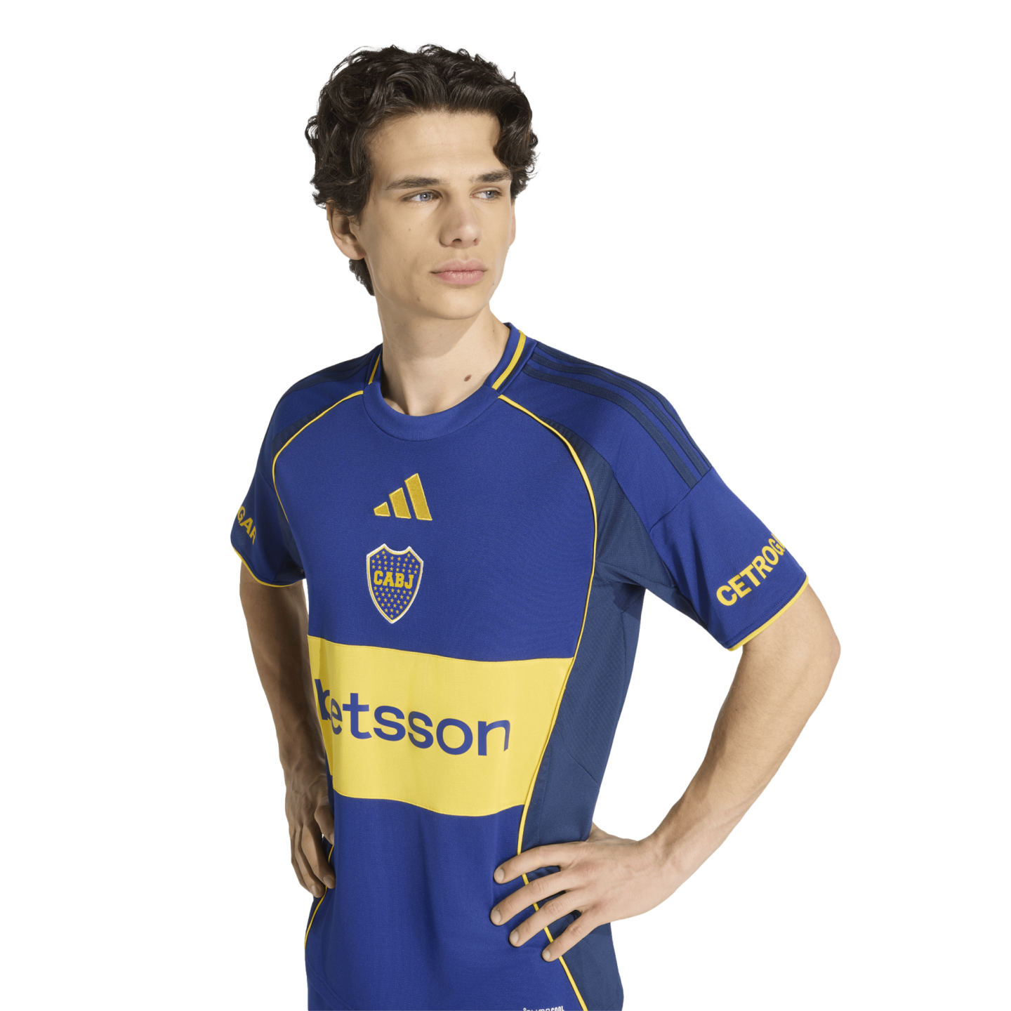 A young man models a blue and yellow Adidas Boca Juniors soccer jersey, standing with hands on hips against a white background.
