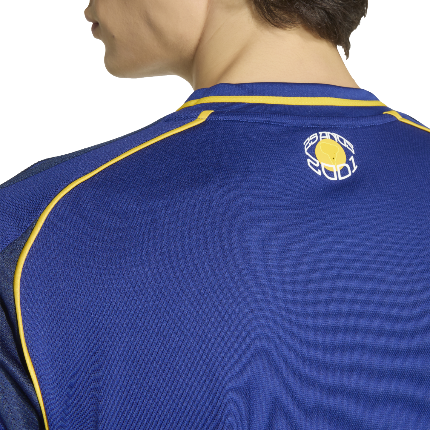Back view of a person wearing a blue athletic jersey with yellow trim and a small logo on the neck that reads "25 ANOS 2001".