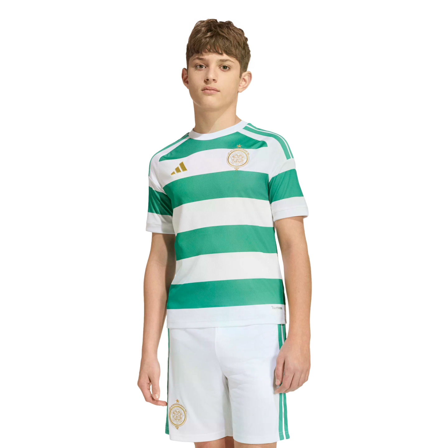 A young person modeling a Celtic FC soccer kit with green and white hoops, gold logos, and white shorts against a plain white background.