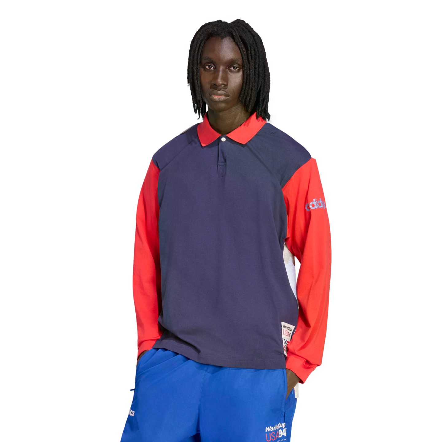 A person with dreadlocks models a navy and red long-sleeve Adidas polo shirt and blue athletic pants, both featuring "World Cup USA 94" branding, set against a solid black background.