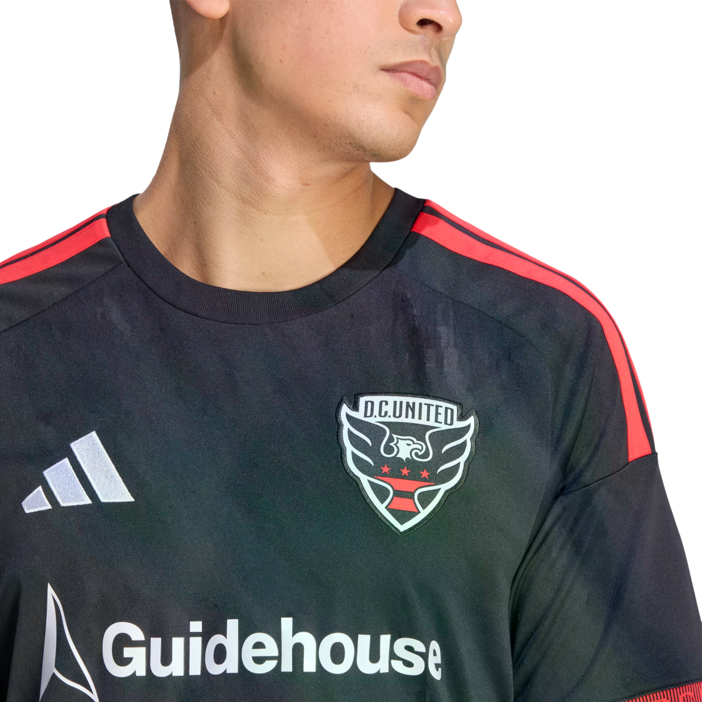 Close-up of a person wearing a black D.C. United soccer jersey with red shoulder stripes, featuring the team crest, white Adidas logo, and Guidehouse sponsor logo.