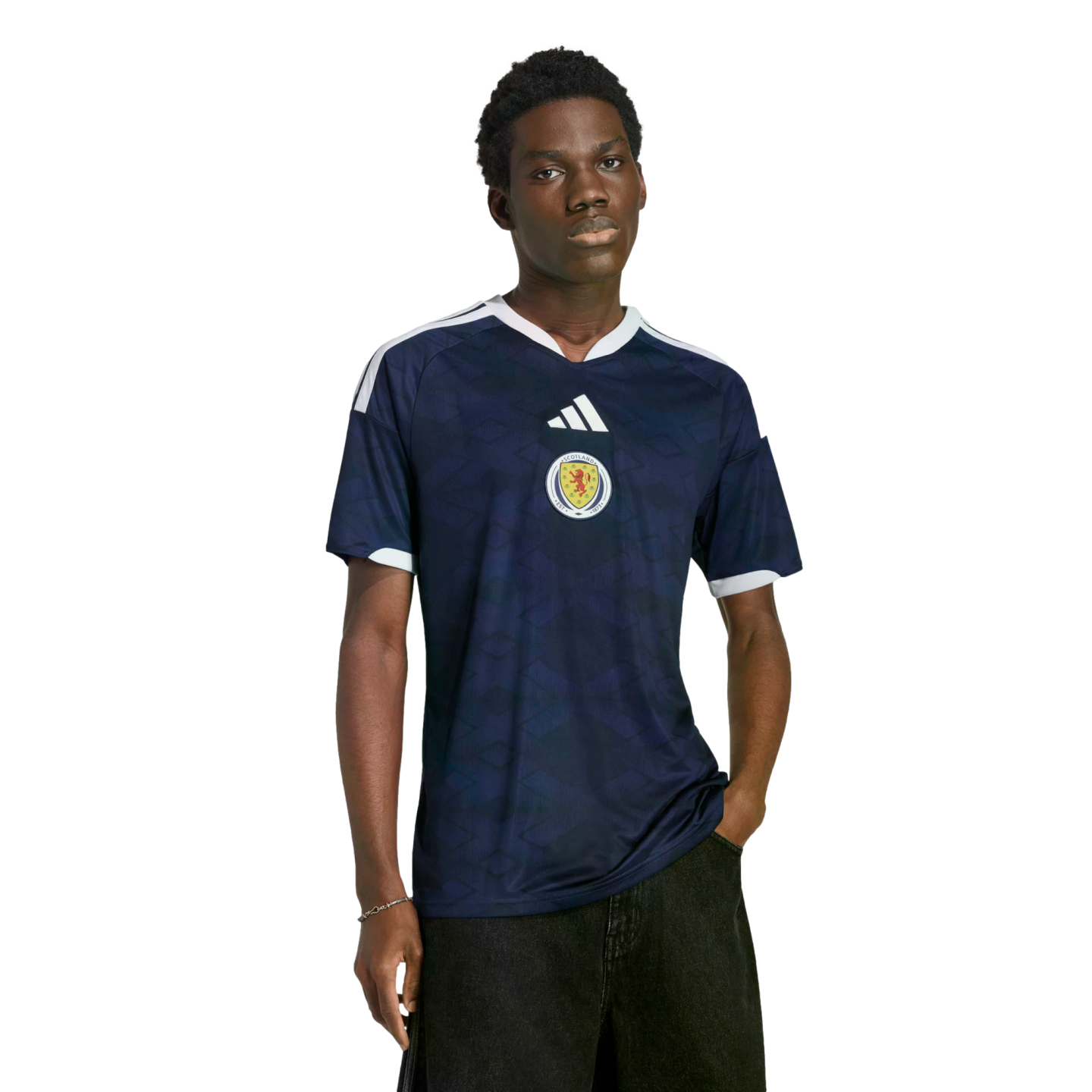 A young Black man models a navy blue Adidas Scotland soccer jersey against a solid black background.
