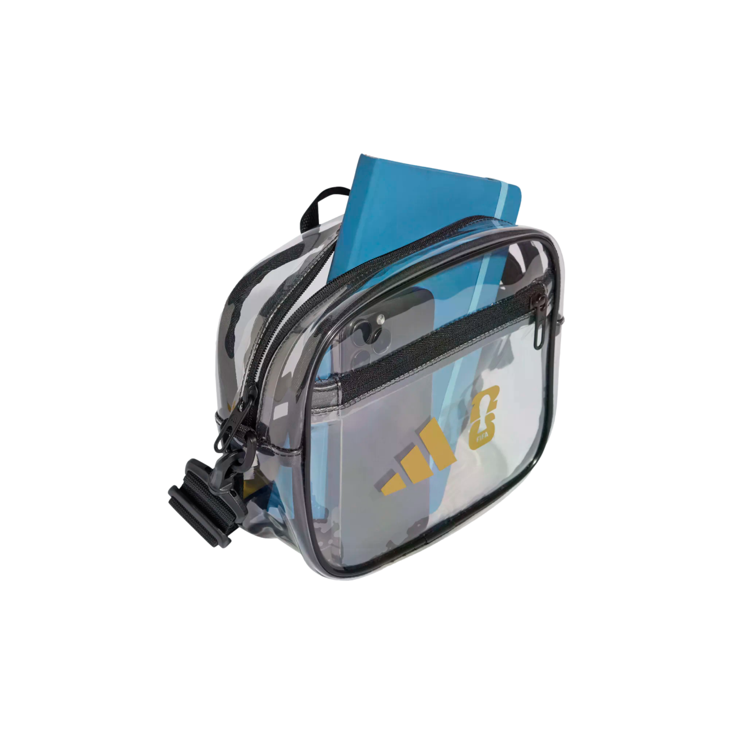 Transparent Adidas crossbody bag holding a blue notebook and smartphone, featuring gold logos. Isolated on a black background.