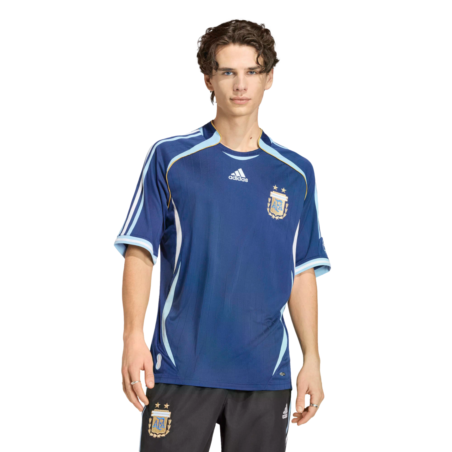 A man wearing a dark blue Adidas Argentina national team soccer jersey and black shorts against a solid black background.