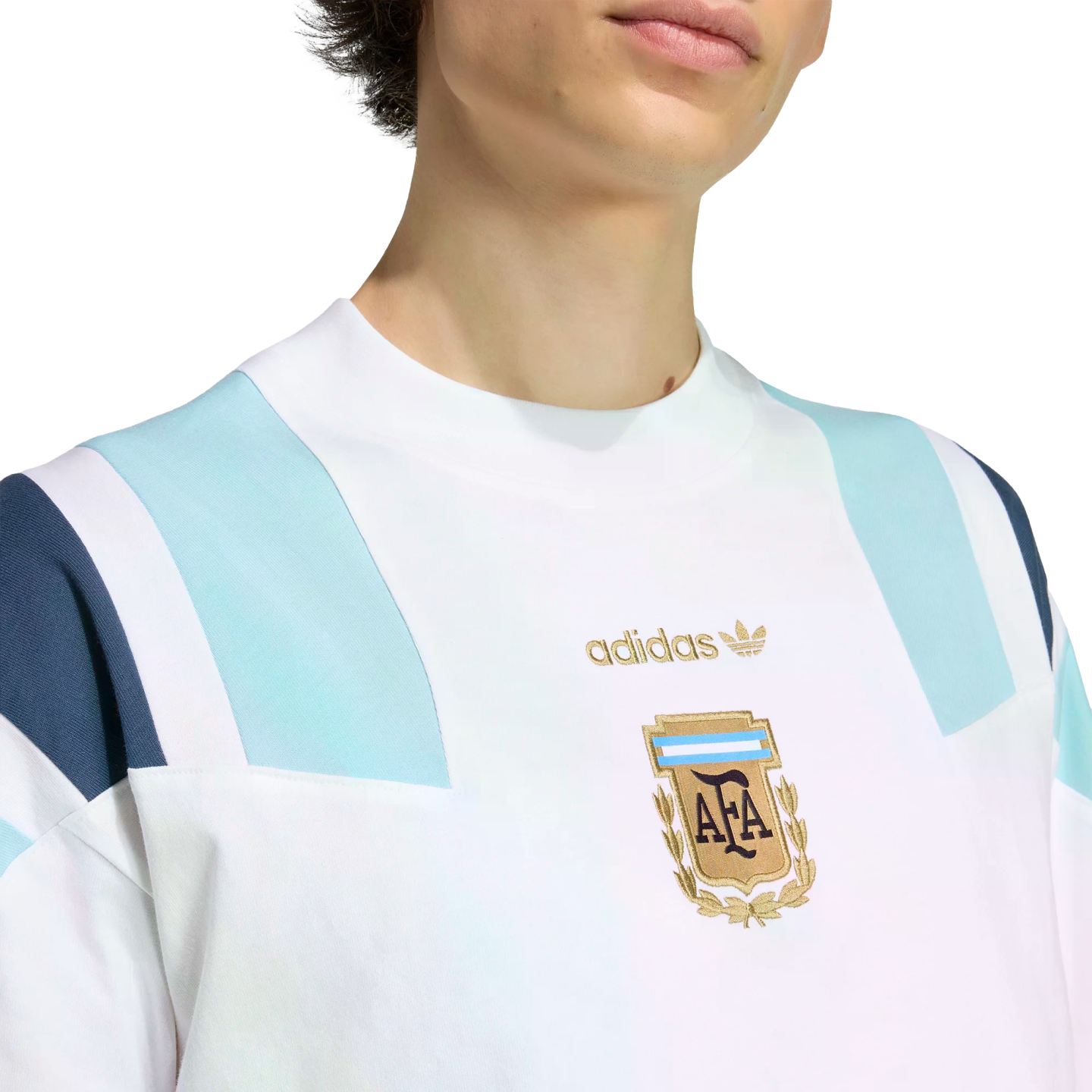 Close-up of a white Adidas sweatshirt featuring light blue shoulder panels and a gold embroidered Argentina Football Association (AFA) crest on the chest.