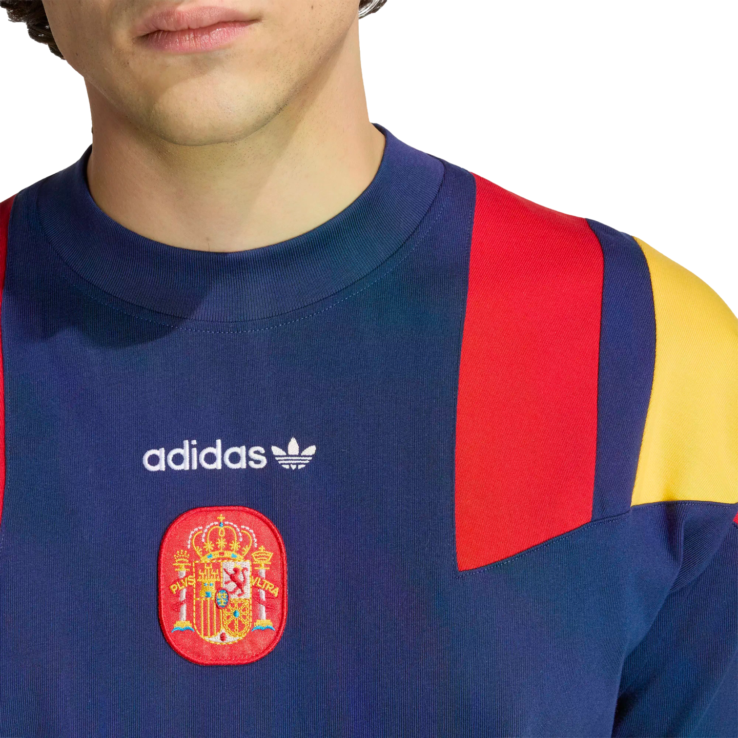 Close-up of a navy blue Adidas sweatshirt with red and yellow shoulder panels and the Spanish national football team crest on the chest.