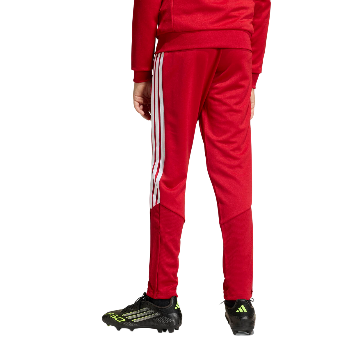 Rear view of a person wearing a red tracksuit with white stripes on the legs and black soccer cleats.