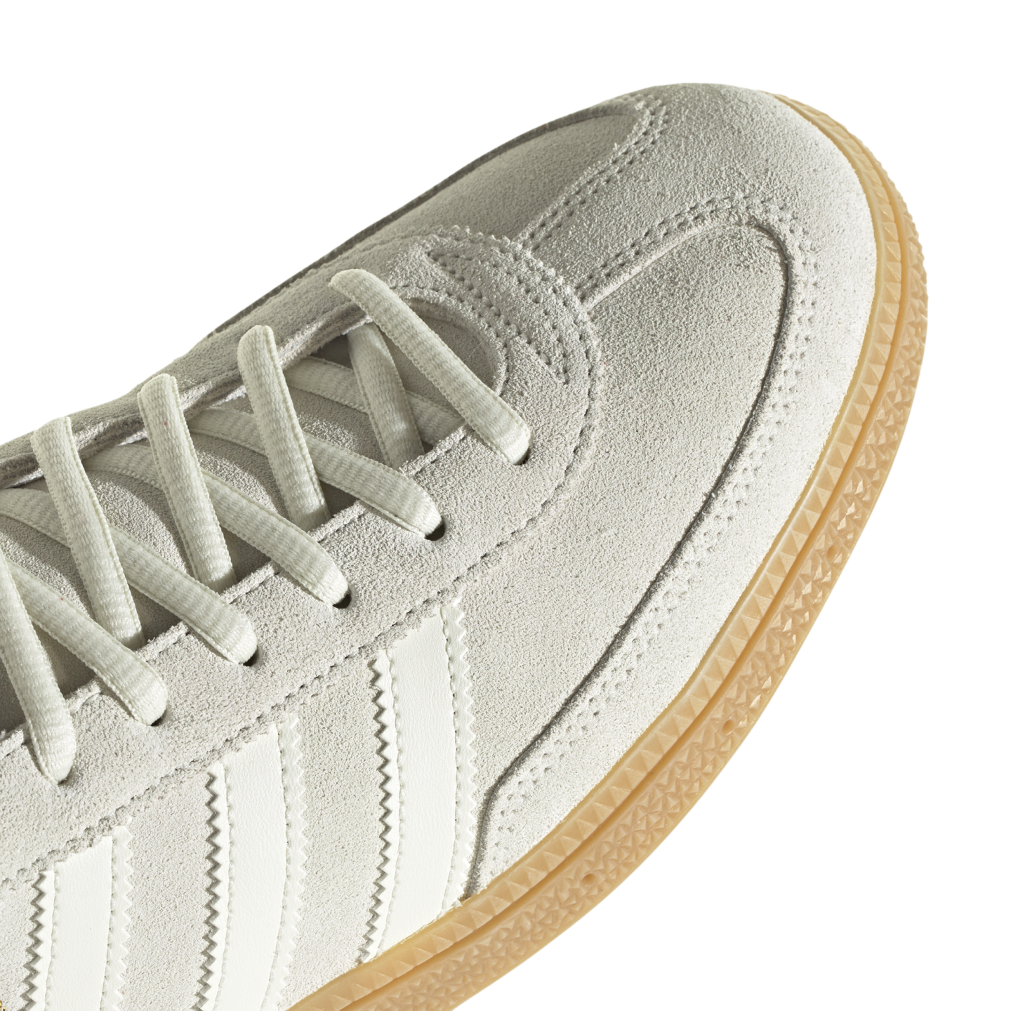 Close-up of a light grey suede sneaker with white laces, side stripes, and a textured gum rubber outsole.