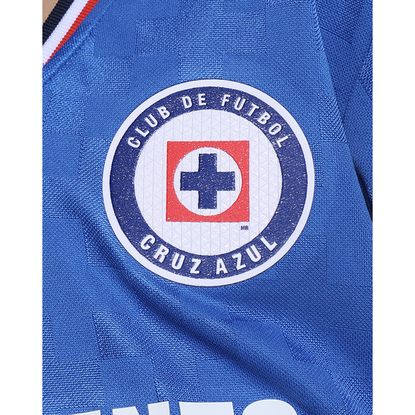 Close-up of the Cruz Azul soccer club crest on a textured blue jersey. The circular logo features a blue cross inside a red square and the team name.