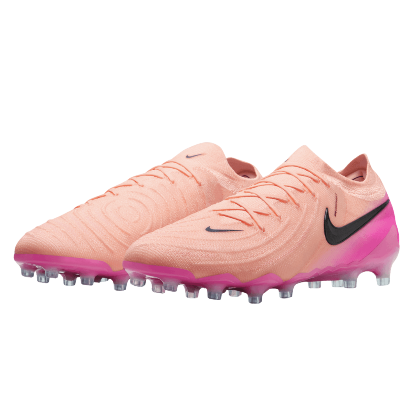 A pair of peach-colored Nike soccer cleats with a textured upper, black swoosh, and vibrant pink sole, set against a black background.