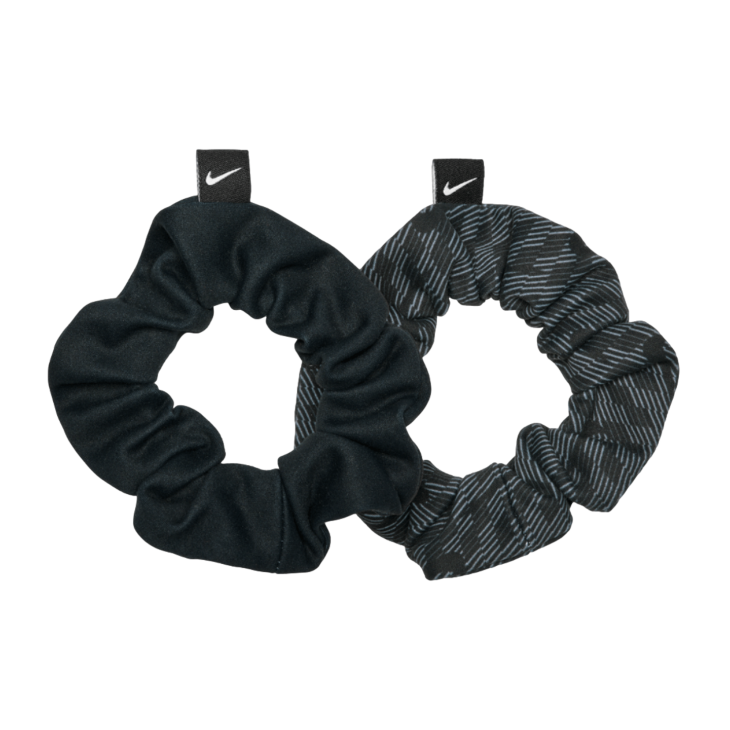 Two Nike hair scrunchies on a black background. One is solid black and the other has a dark grey patterned design. Both feature a small tag with a white swoosh logo.