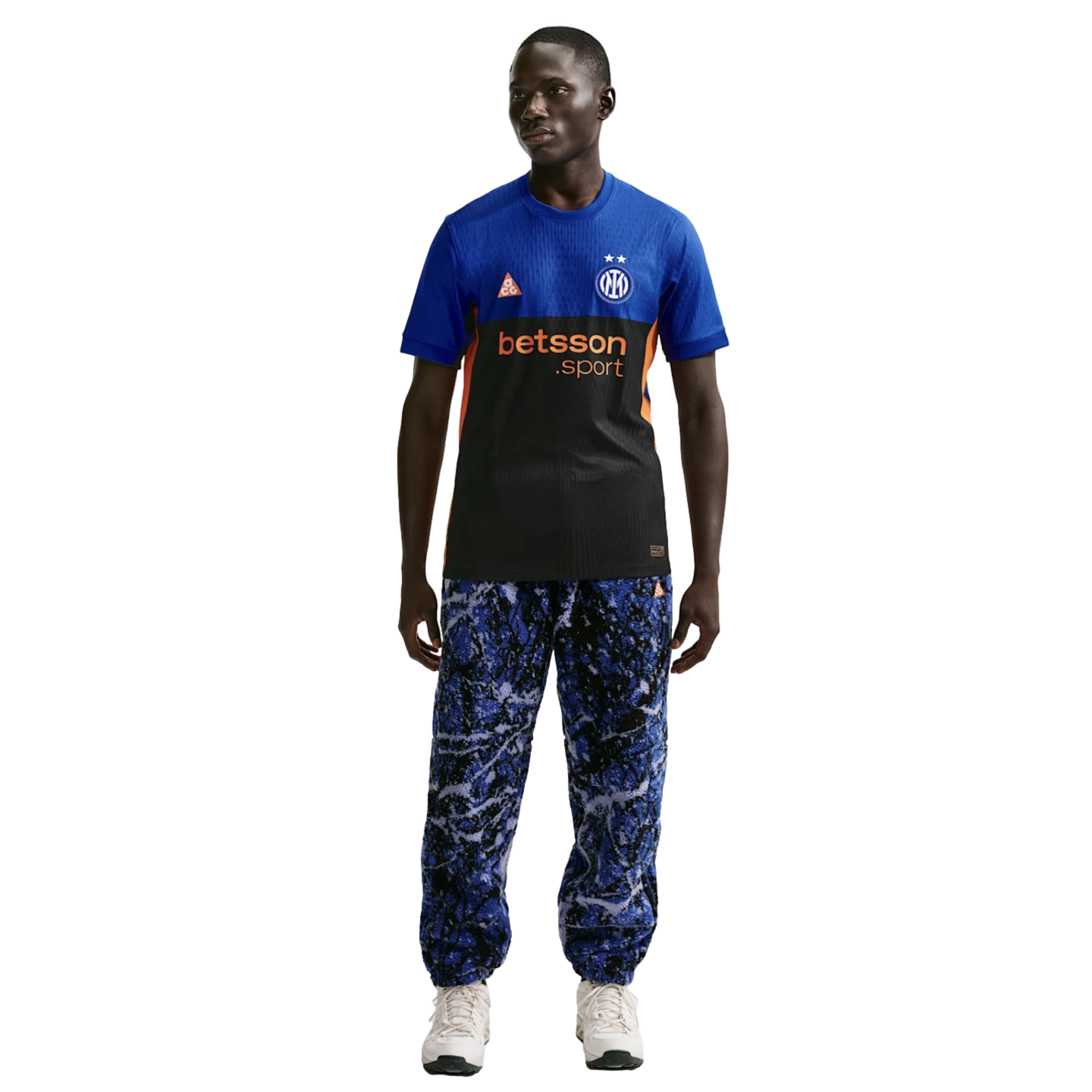 A man wearing a blue and black Inter Milan jersey, blue marble-patterned joggers, and white sneakers, standing against a solid black background.