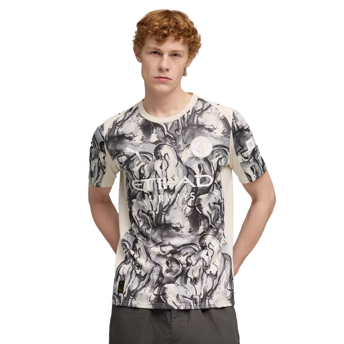 Man with curly red hair wearing a white and black marble-patterned soccer jersey with the Etihad Airways logo, posed against a solid black background.