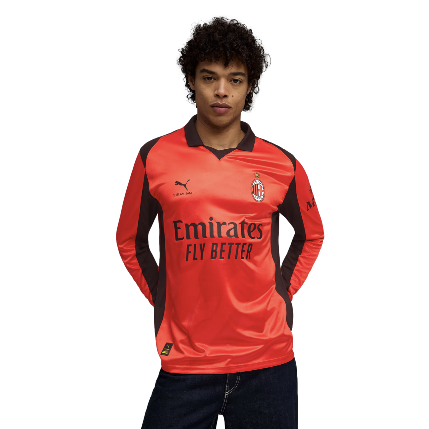 A person with curly hair wearing a long-sleeved, bright orange AC Milan soccer jersey with dark brown accents against a black background.