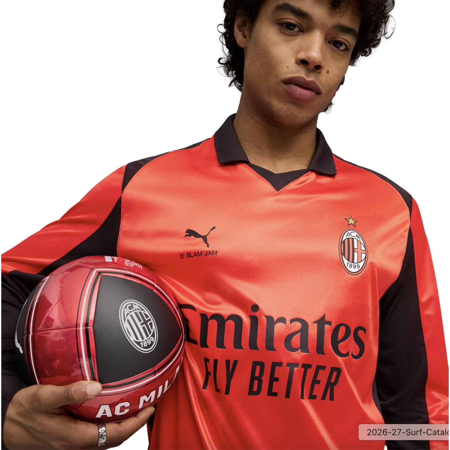 A man wearing an orange Puma AC Milan soccer jersey holds a matching soccer ball against a black background.