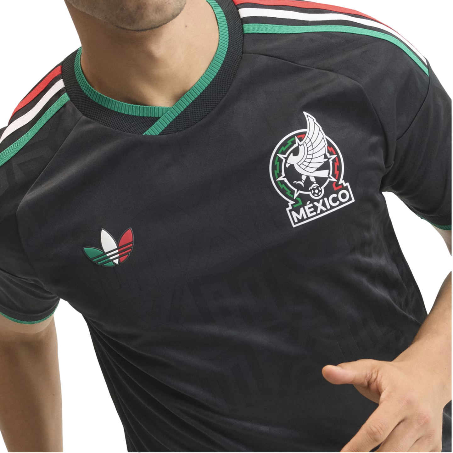 Close-up of a person wearing a black Mexico football jersey with green, white, and red accents, the national team crest, and a colorful Adidas trefoil logo.