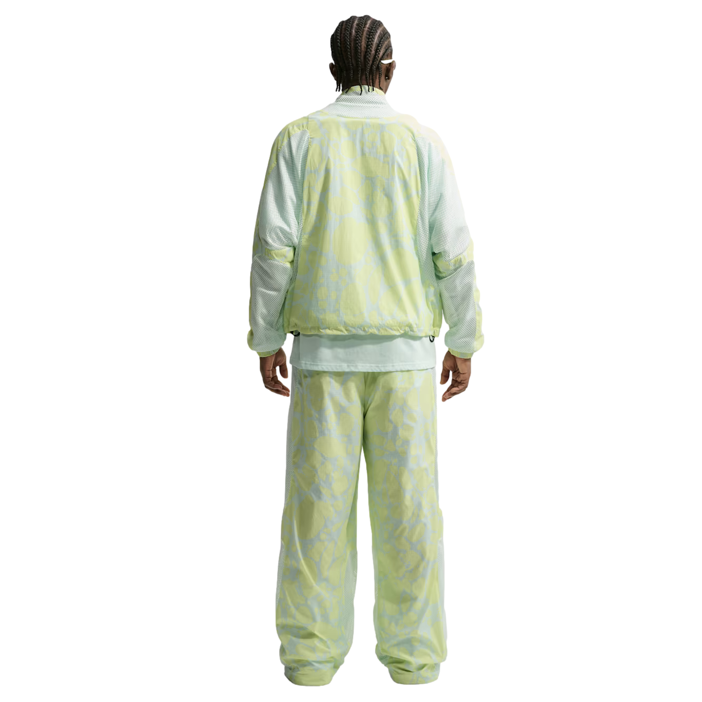 Rear view of a person with braided hair in a light green and yellow marbled-print tracksuit. The loose-fitting jacket and pants feature mesh paneling on the sleeves and sides.