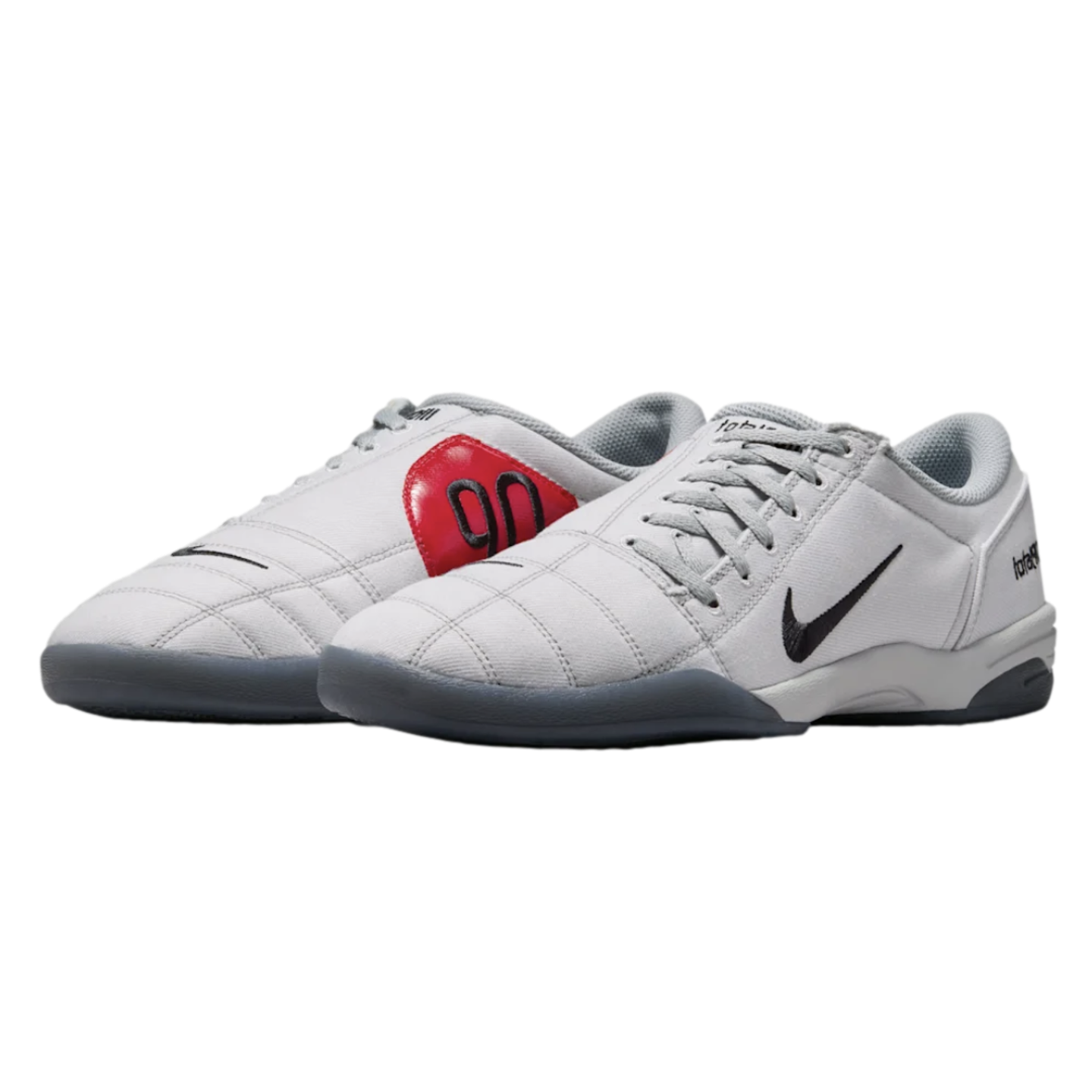 A pair of light grey Nike Total 90 indoor soccer shoes featuring a distinctive red "90" circular logo and a black Nike Swoosh.
