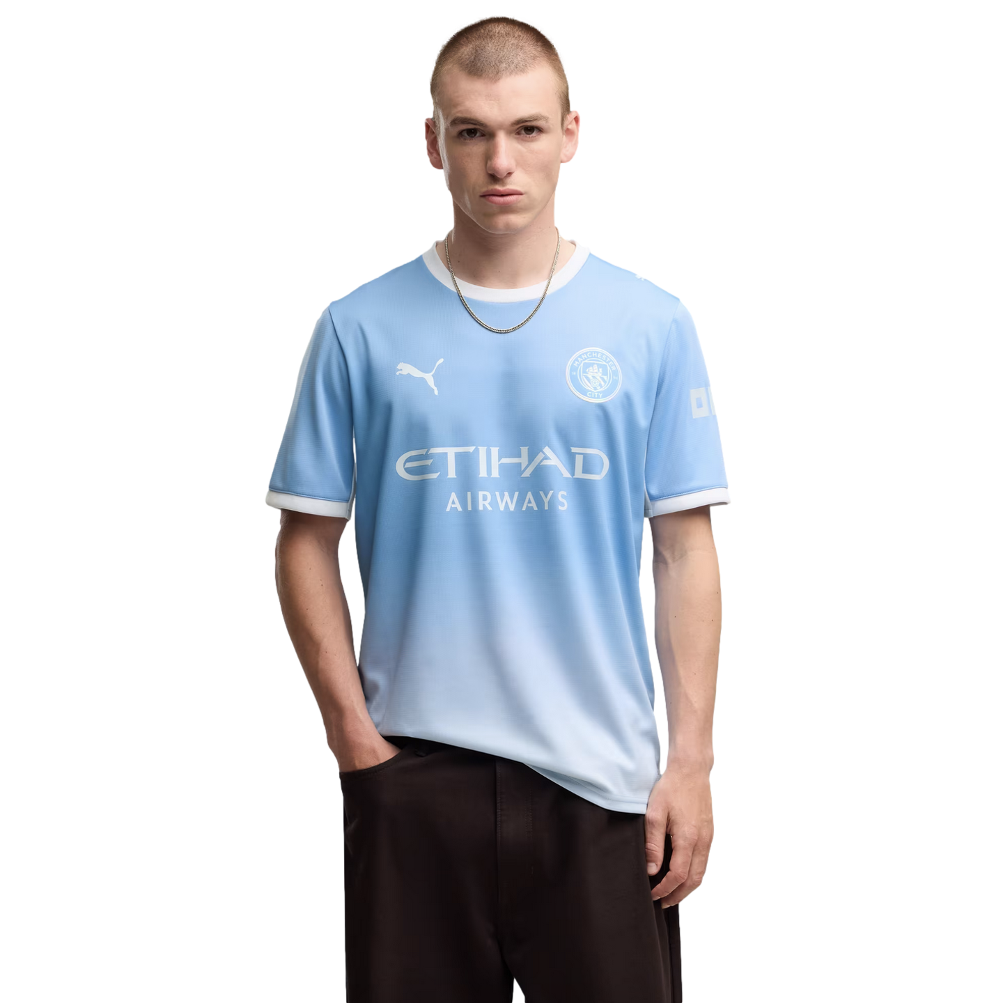 A man wearing a light blue Manchester City soccer jersey and dark pants, posing against a plain white background.