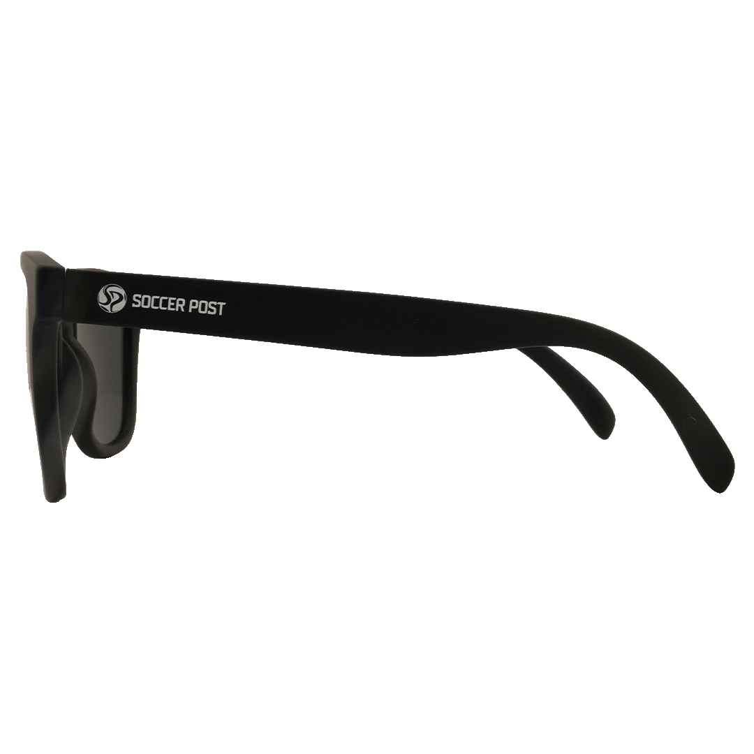 Side view of matte black sunglasses with white "SOCCER POST" text and logo on the temple, displayed against a solid green background.